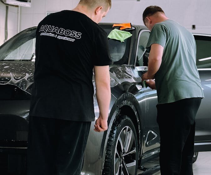 Two men detailing a car in an indoor workshop, focusing on precision and care.